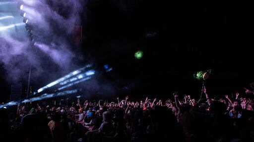 A wide photo of the crowd at night with concert lights in the air.