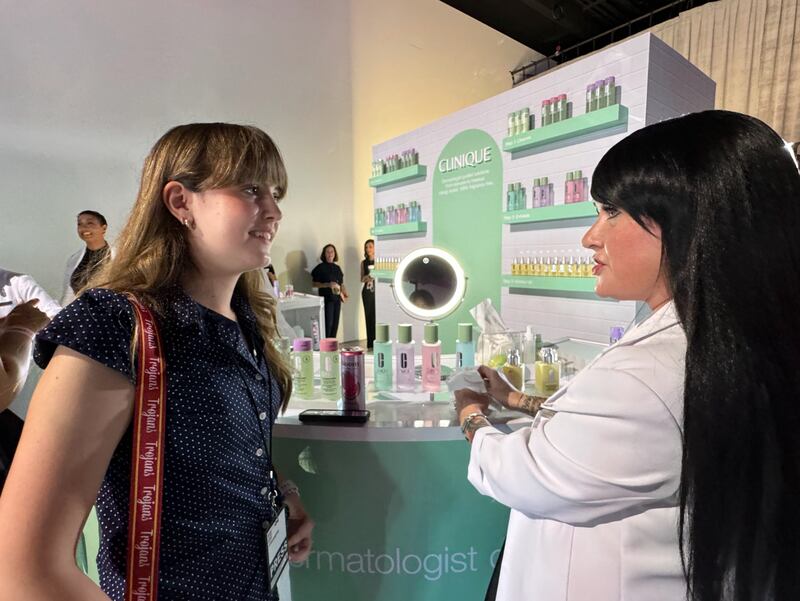 A Clinique skin worker is wearing a white coat while explaining skincare to an attendee.