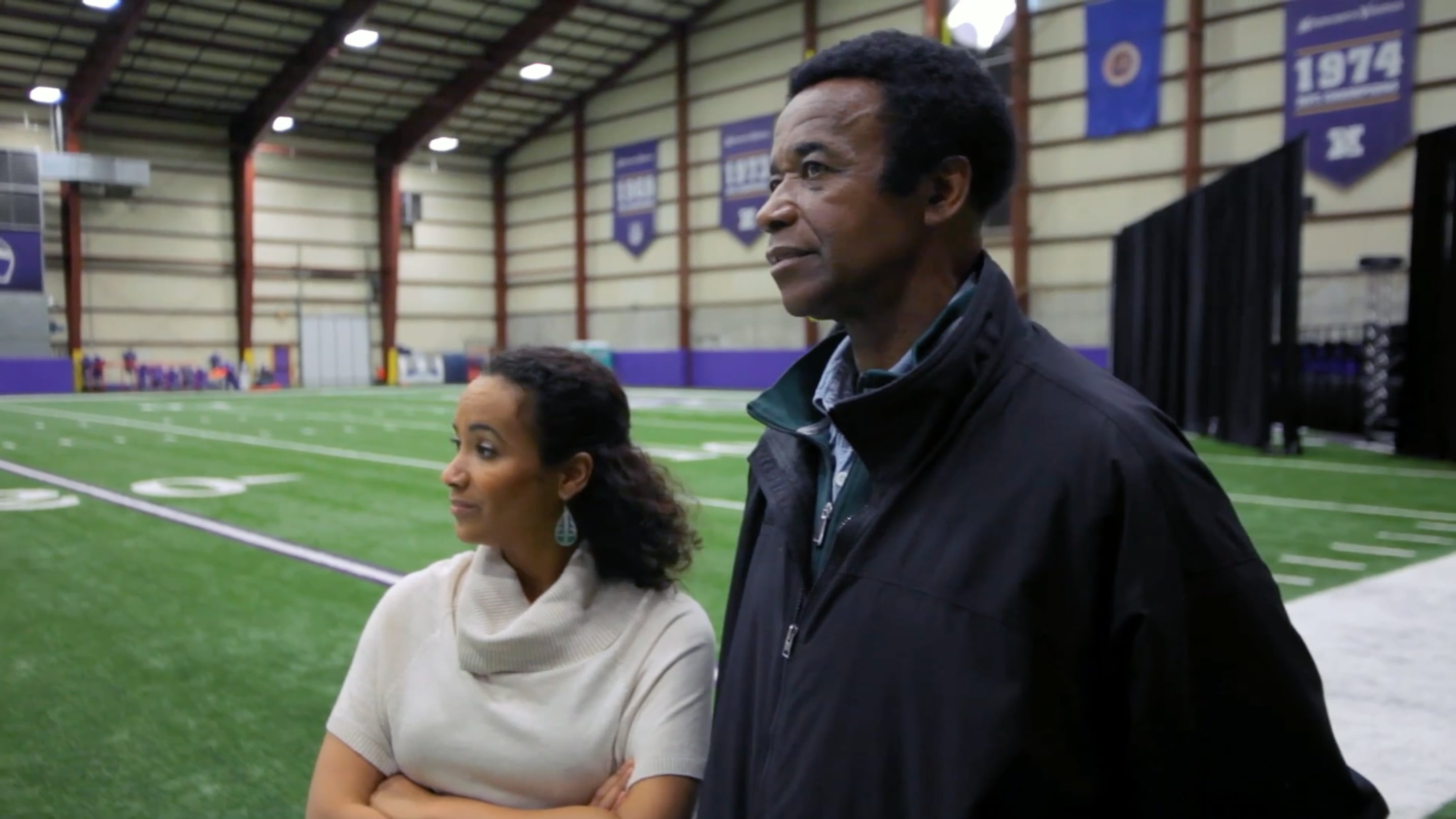Maya Washington standing inside a football practice facility to the left of her father, Gene Washington