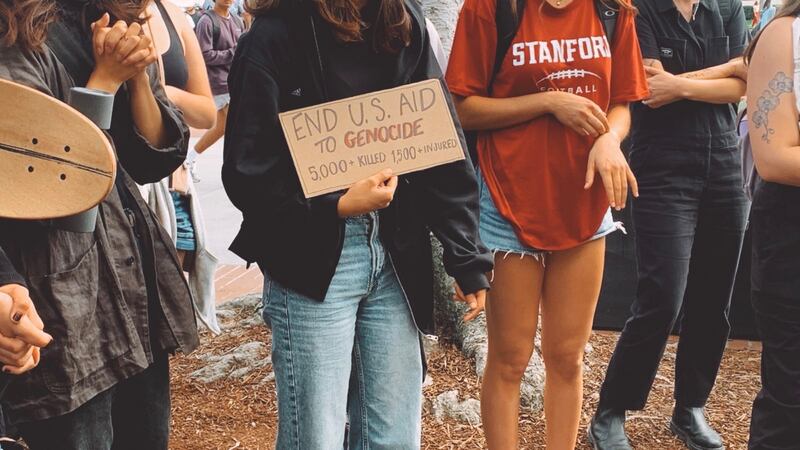 A student holds a sign reading ‘End U.S. Aid to Genocide. 5000 killed 1500 injured.’ Citing a death toll from a few days prior.