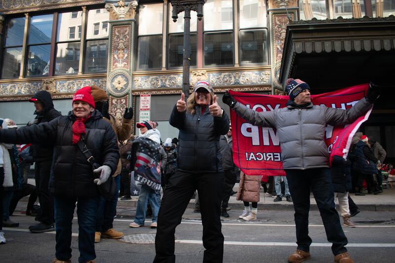 A picture of three people in Trump merchandise standing on a street.
