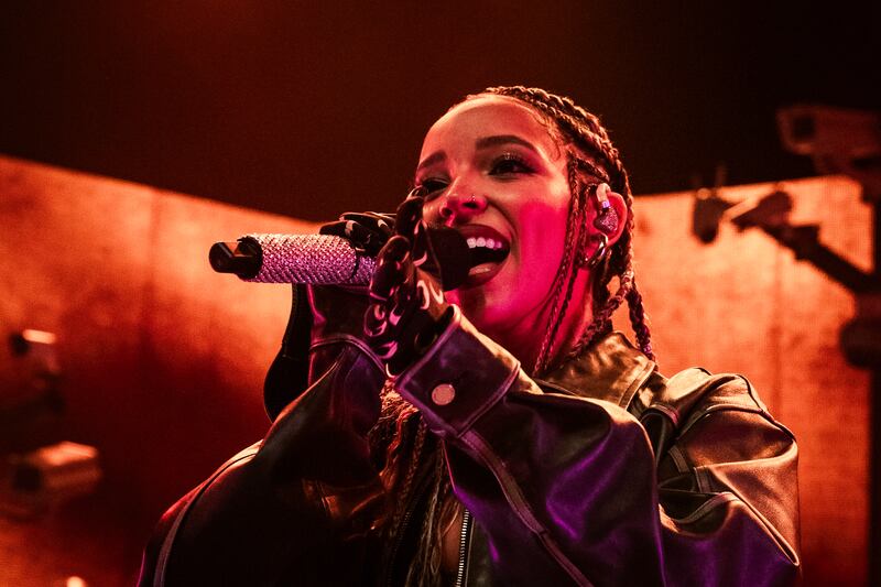Photo of a woman singing into a microphone in front of an orange backdrop