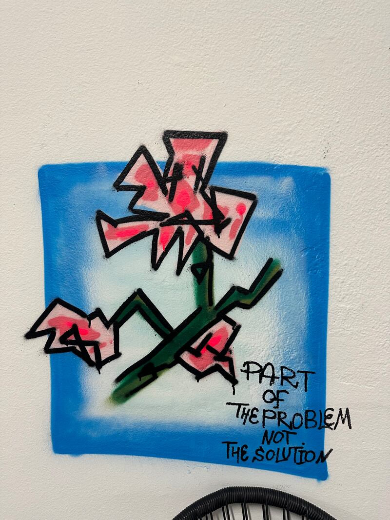 Spray-painted rigid pink tulips on Sheeha's wall. Writing says "part of the problem not the solution".