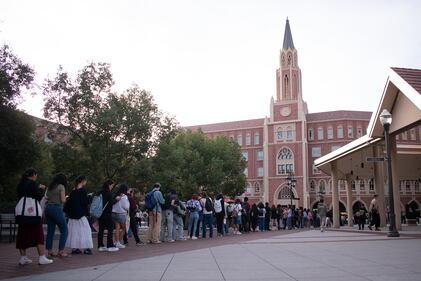A long line of people in front of a brick-colored building waiting to cast their votes.