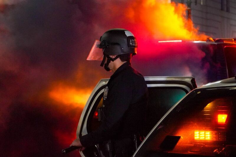 [Photo of police officer in front of brightly colored smoke.]