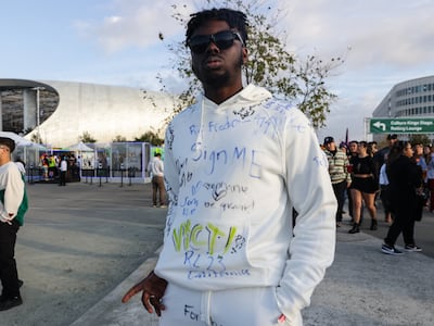 A photo of a fan wearing a white sweatshirt with names signed on it with markers.