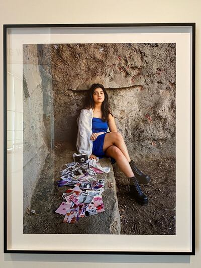 A photo of a young woman sitting in a rocky setting with old photographs, a camera and a scarf scattered in the foreground.