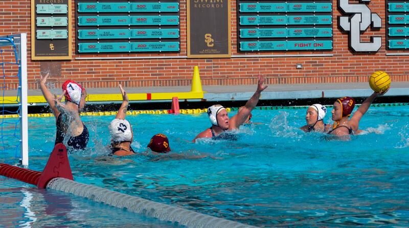 A photo of Emily Ausmus, wearing a red No. 9 USC cap, lining up a shot with multiple Irvine players sticking their arms to attempt to block it.