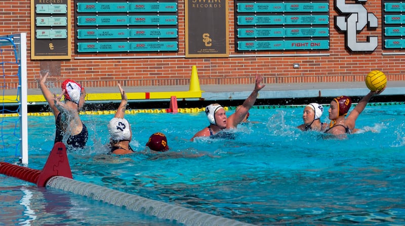A photo of Emily Ausmus, wearing a red No. 9 USC cap, lining up a shot with multiple Irvine players sticking their arms to attempt to block it.