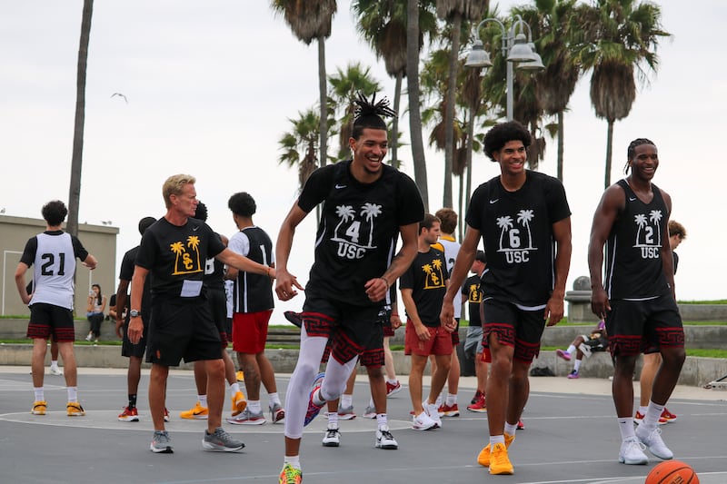 Baker-Mazara (4), Jacob Cofie (6) and Ezra Ausar (2) smile on a basketball court at Venice Beach. They wear black and white USC tee shirts adorned with palm trees.