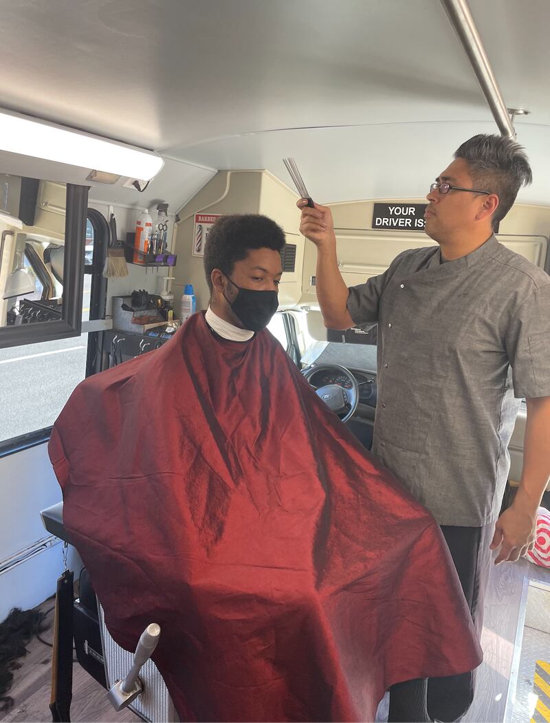 "A photo of Hector Trinidad standing above USC student and customer Jackson Sutherlin, preparing to give him a haircut."