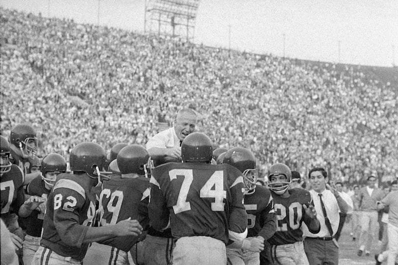 Coach John McKay of Southern California, center, is carried off the field by his happy players after they beat Notre Dame, 20-17. The photo is in black and white.