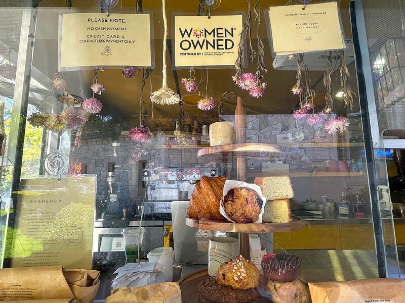 A photo of the display window, with pastries and flowers behind the glass, and the certification that says "Women Owned."