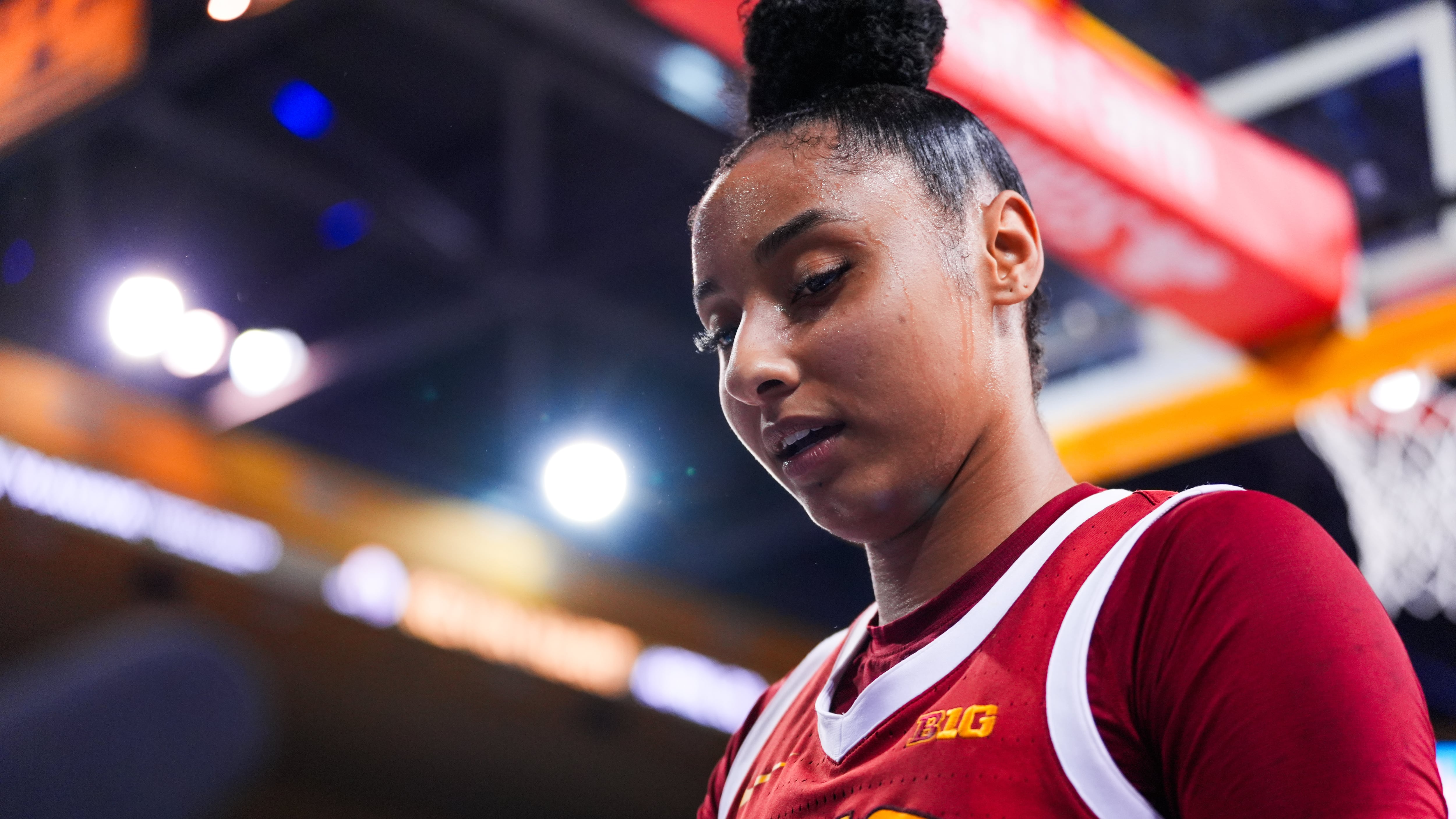 JuJu Watkins stands in profile above the camera looking down. She wears a cardinal USC basketball jersey with gold lettering and a cardinal short-sleeved shirt underneath.
