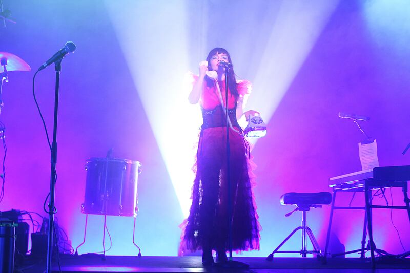Photo of a woman holding a rotary telephone next to a keyboard on a stage