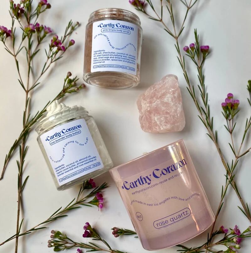 Photo of a body butter, a candle, and body scrub surrounded by flowers.