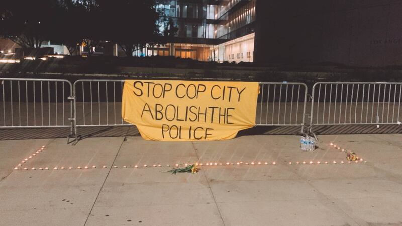 [Photo of banner reading "Stop Cop City / Abolish the Police" with candles and flowers out front of LAPD HQ.]