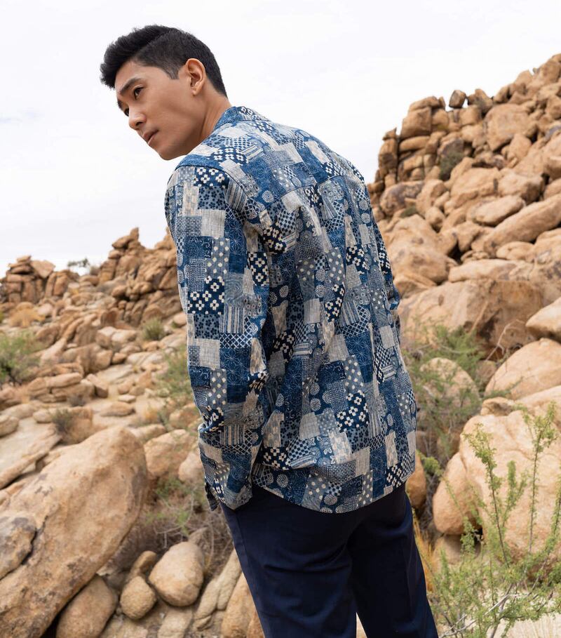 A man stands in front of rocks with his back turned to the camera