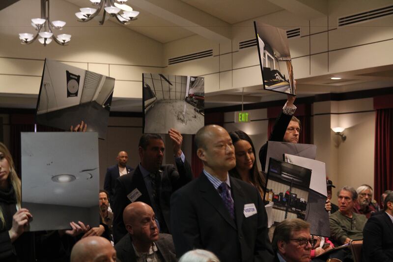 Several employees from Helinet hold photographs of leaking ceilings at their workplace, claiming they need to be granted the lease to do necessary maintenance and upgrades, on Feb. 8, 2024
