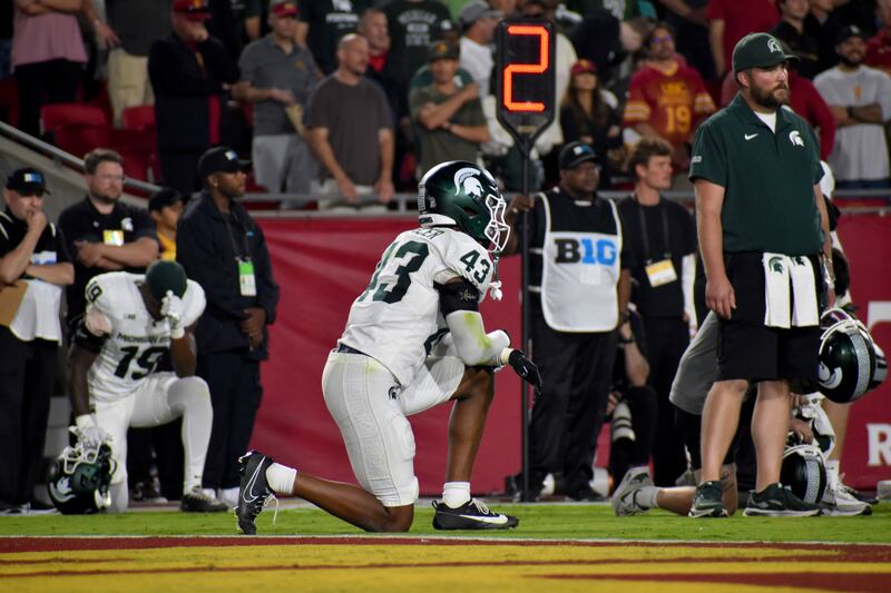 Malik Spencer (43) kneels on the field. He wears a white and green MSU football uniform.
