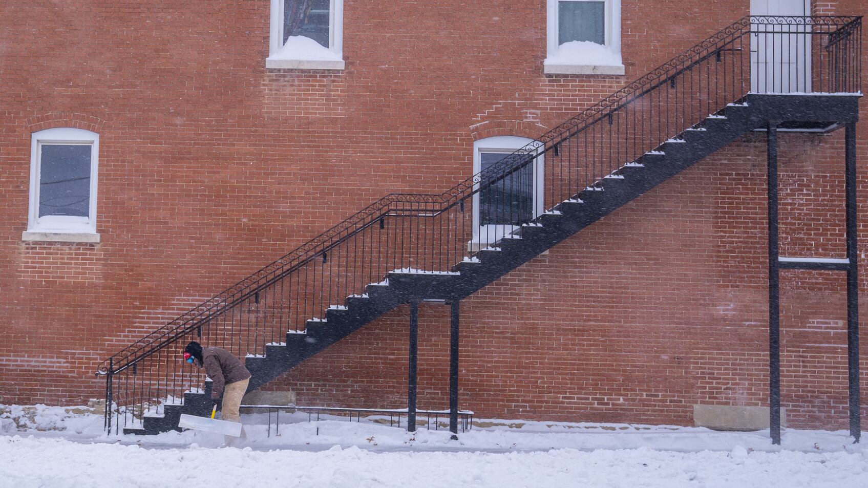 Man shoveling snow in front of a brick building.