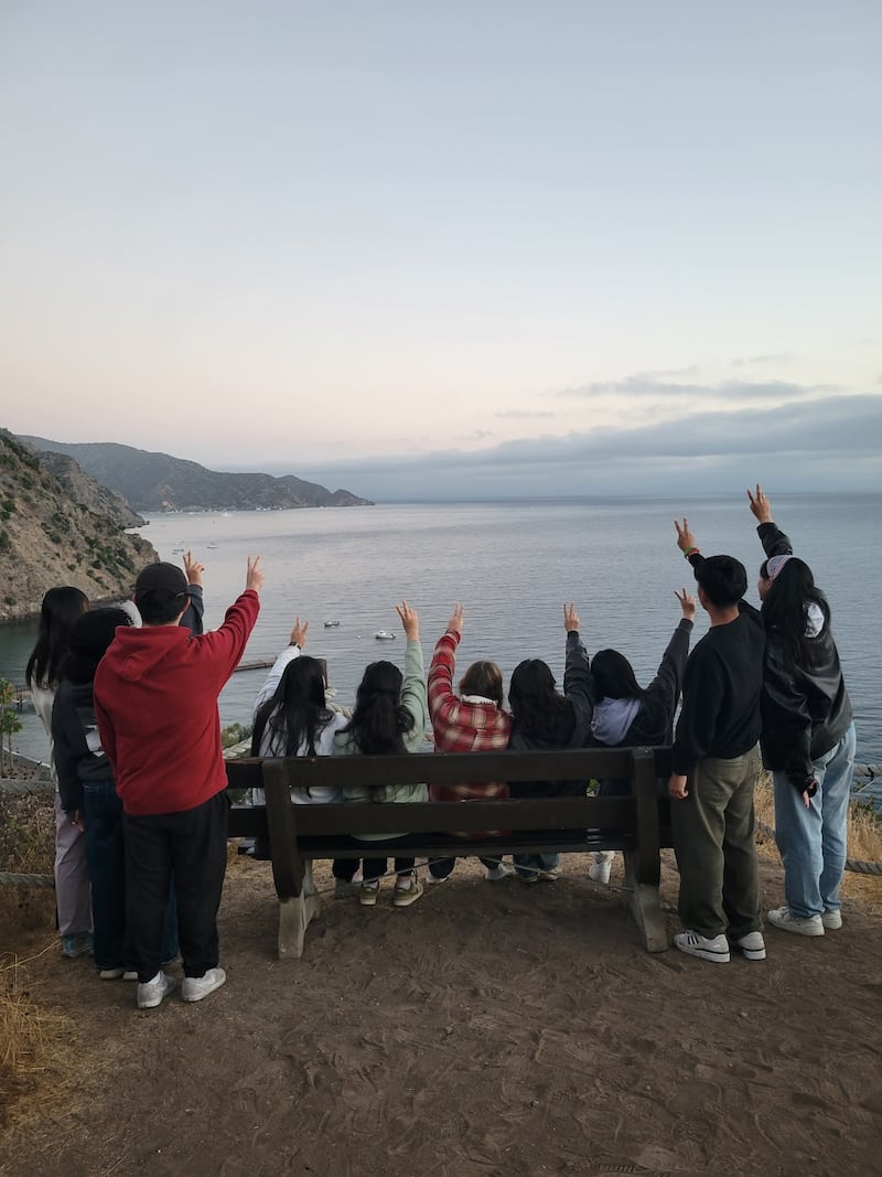 Students raise their hands in the air overlooking the ocean.