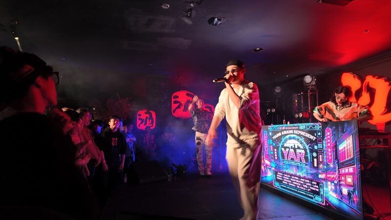Photo of a man in white with a microphone performing in front of a DJ