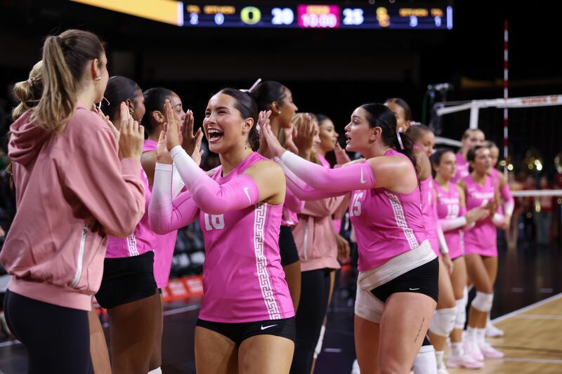 USC women's volleyball players high-five each other with smiles on their faces.