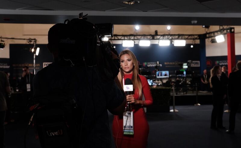 A Vision Latina reporter films a stand up in the media spin room.