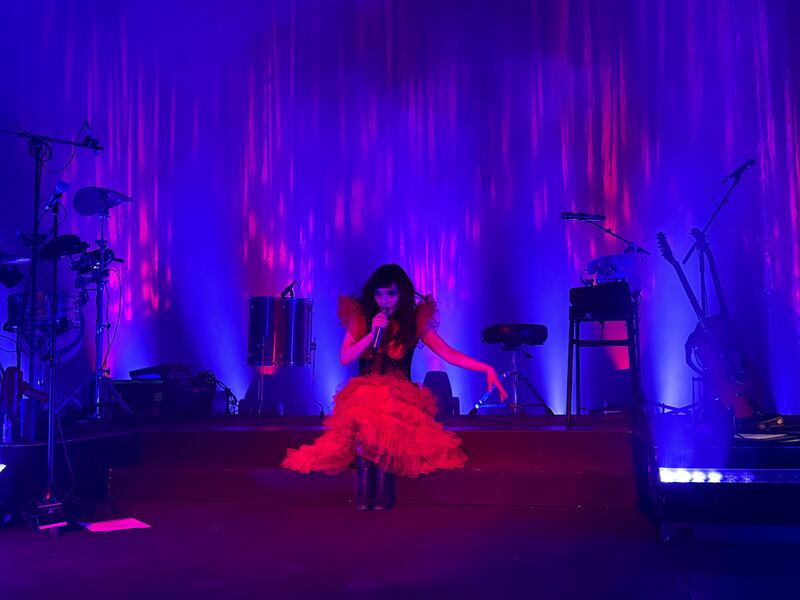 Photo of a woman in a red dress sitting on steps in front of a drum set and a stool