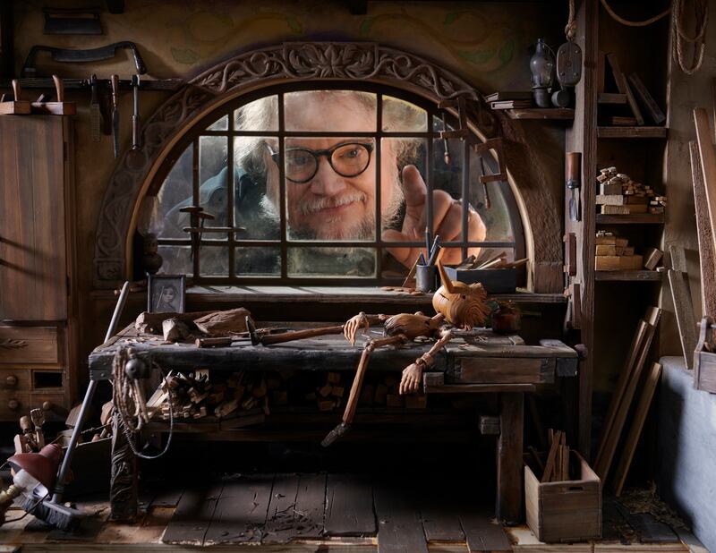 A man looking through a window of a miniature house with a puppet on a table