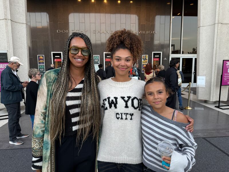 Three attendees stand together outside the Dorothy Chandler Pavilion, smiling at the camera, with one holding a drink.