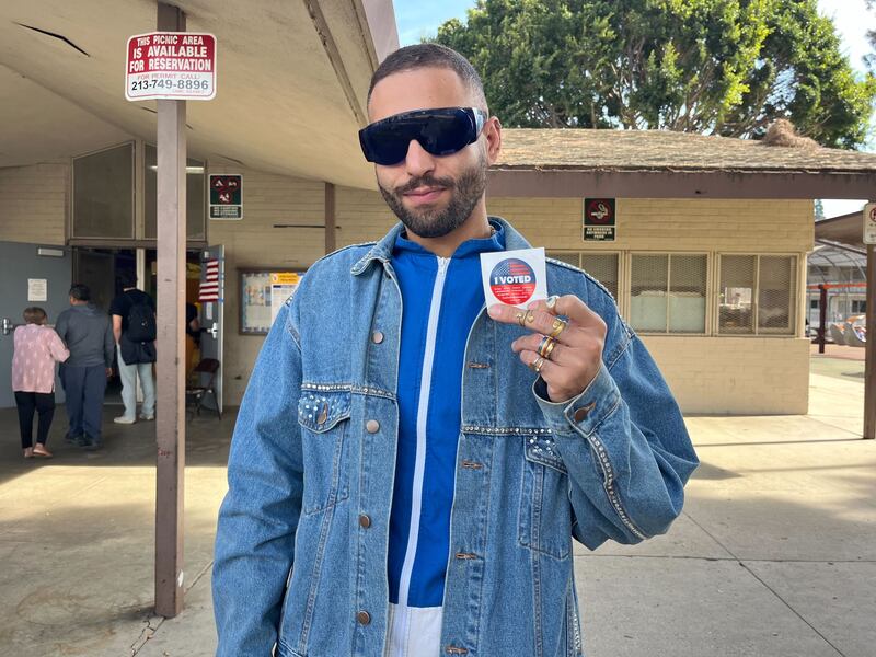 A man with sunglasses holding up an I Voted sticker.