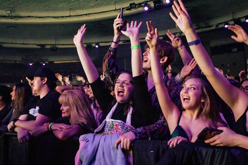 A photo of fans screaming with their hands in the air in the audience at the concert venue.