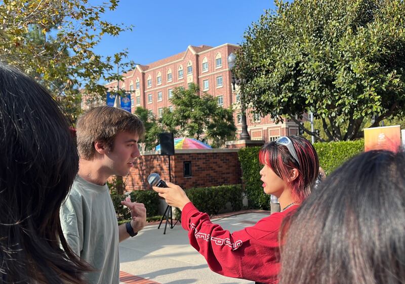 Photo of a man in grey being asked with a microphone by a girl in red