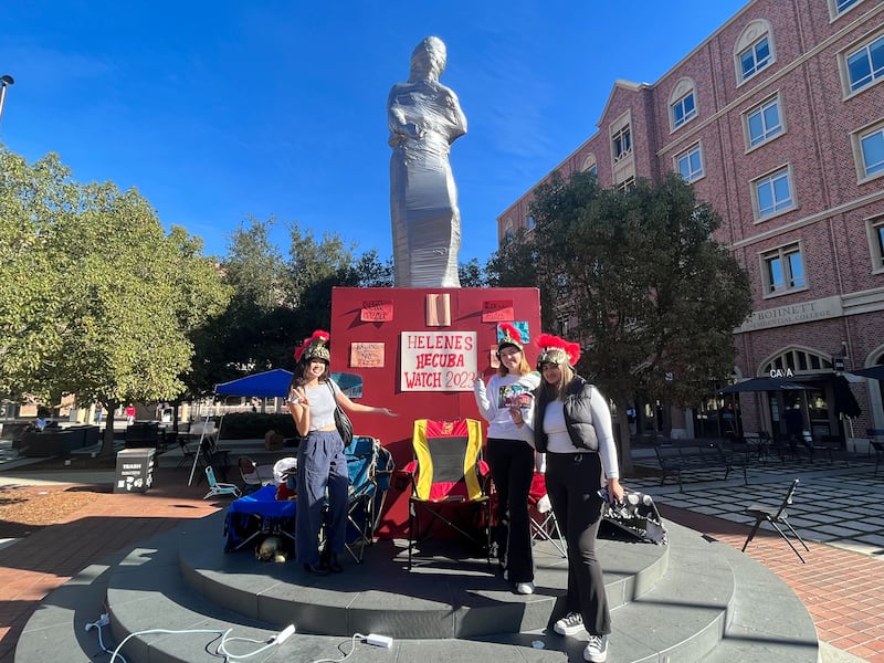 A group of girls stand in front of a statue of a woman that is wrapped in duct tape