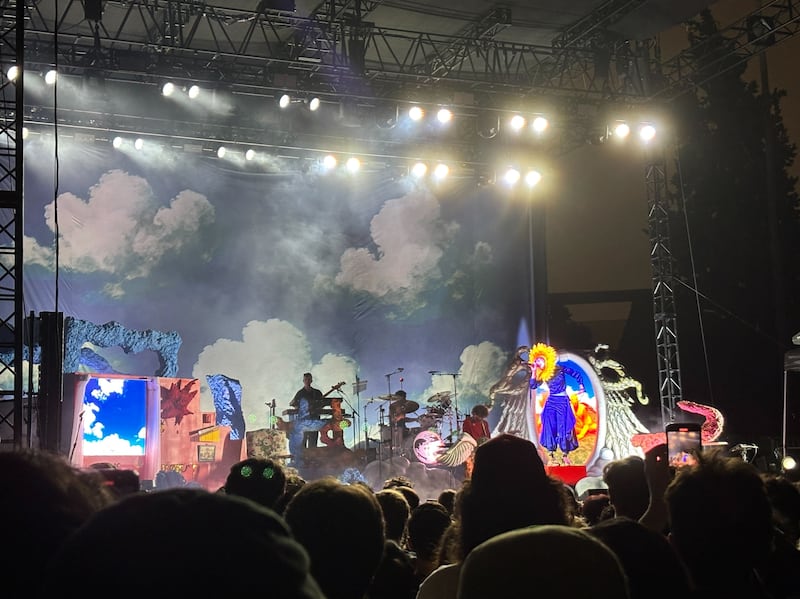 The duo performs in eclectic costumes onstage. The backdrop is a hand painted cloud scheme.