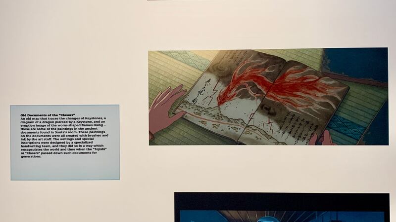 A photo of the exhibit of Makoto Shinkai’s past directorial work featuring a drawing from a film and a text block about the drawing.