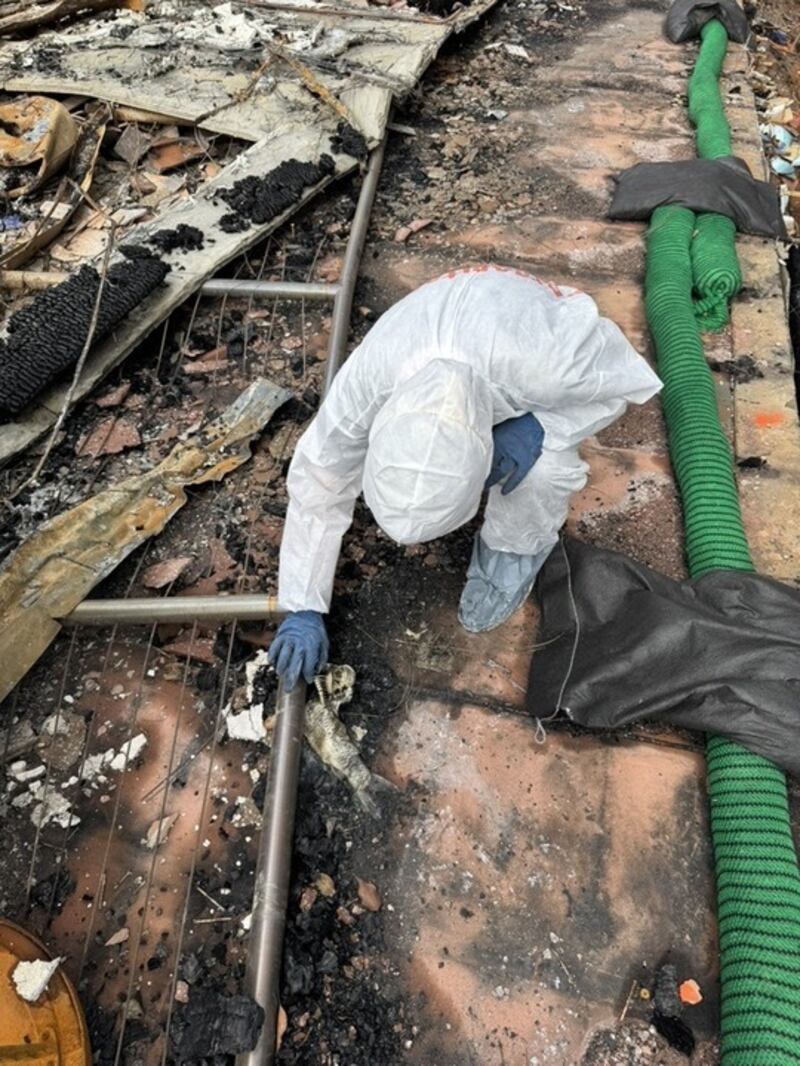 A person in protective gear examines the body of a burnt koi fish in rubble.