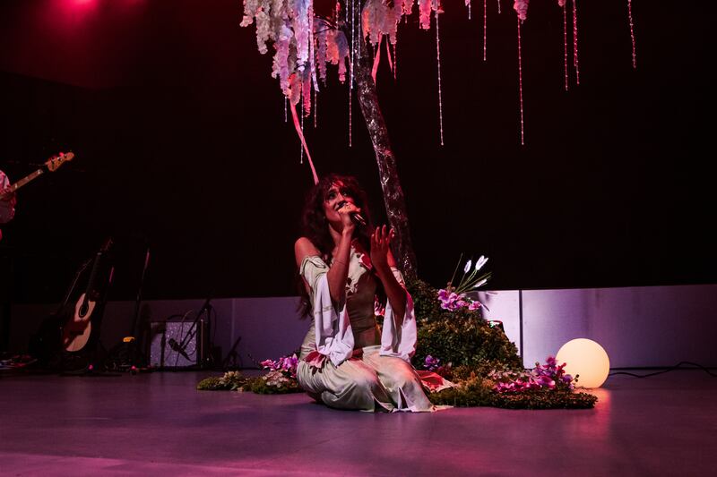 Photo of a woman with a microphone sitting in front of a prop of a tree