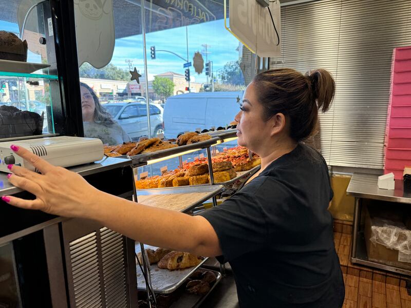 Photo of a woman pressing an intercom to speak with a person on the other side of a glass window