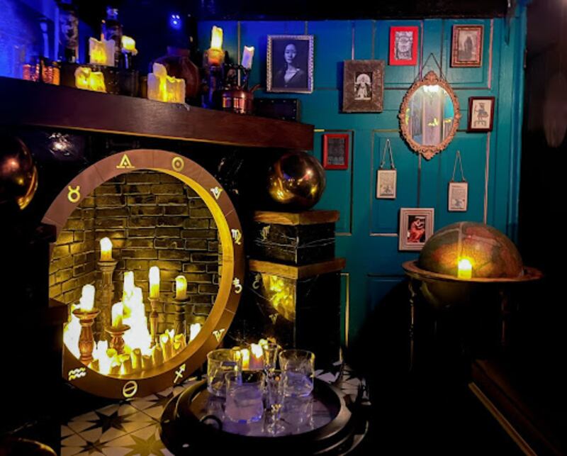 A fireplace filled with LED candles, against a blue wall with old portrait photos on it.