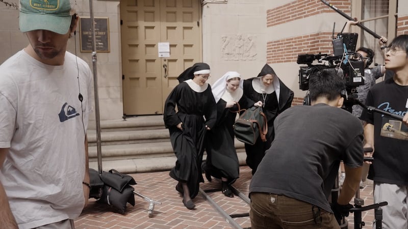 The nuns run forward as a camera tracks them on a rolling shot.