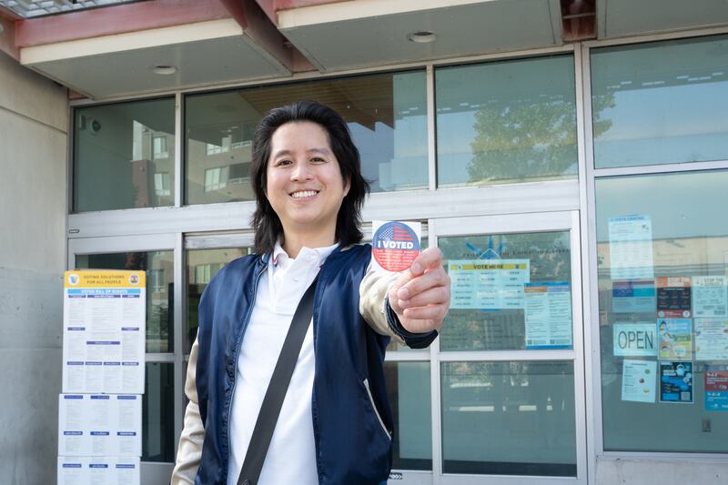Ryan Fung stands in front of the polling station at the Chinatown branch of the Los Angeles Public Library holding an "I Voted" sticker.