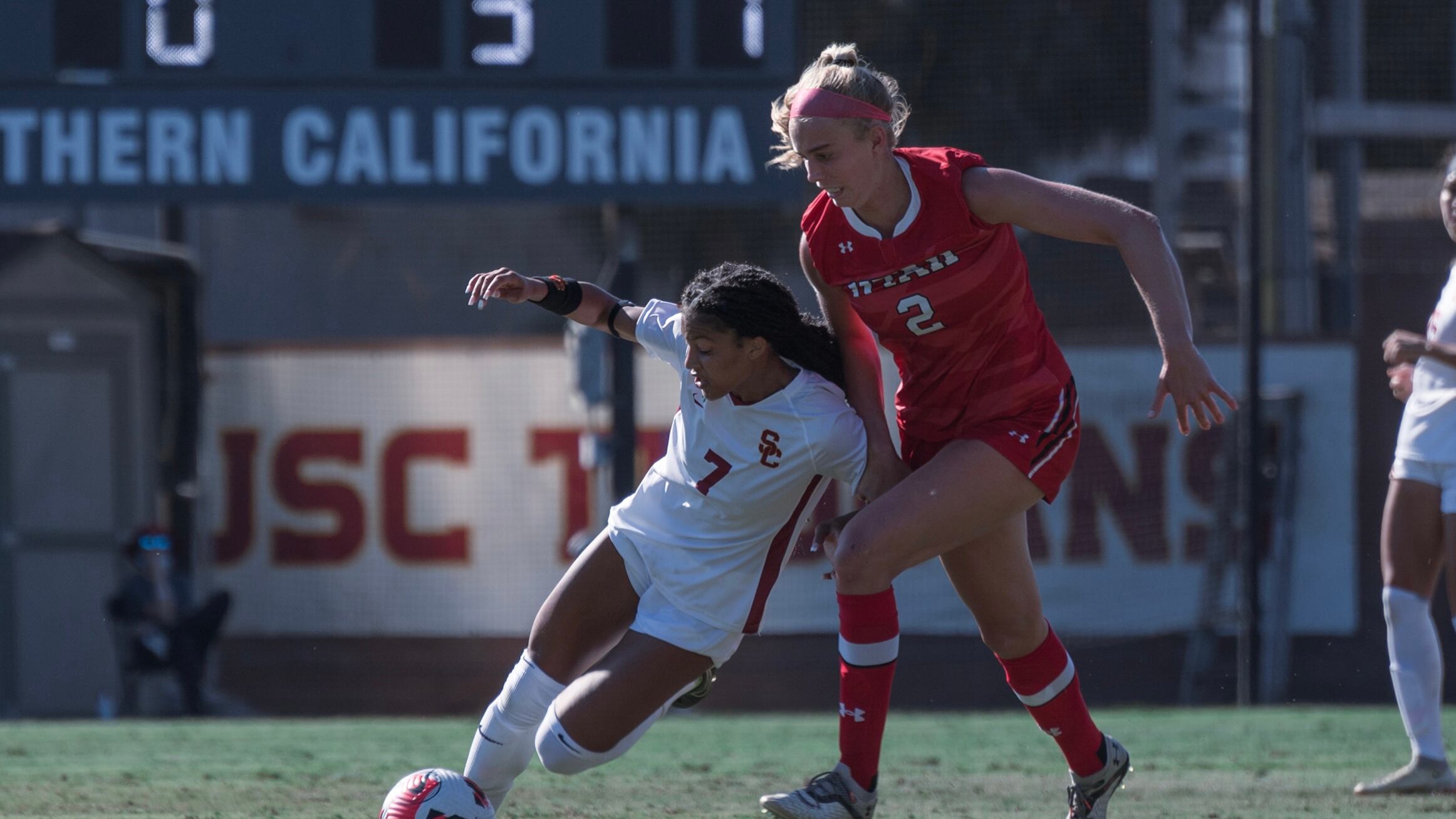 A photo of USC junior midfielder Croix Bethune in a white uniform battling for the ball with a Utah defender in a red uniform.