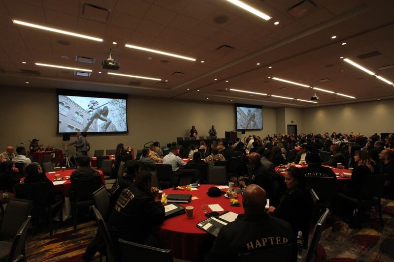 Photo of a room full of tables and people sitting around them looking at two large screens.