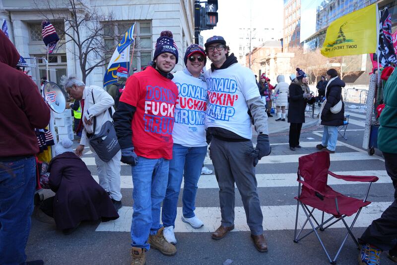 Three men in Donald Trump shirts and hats standing side by side on a street.