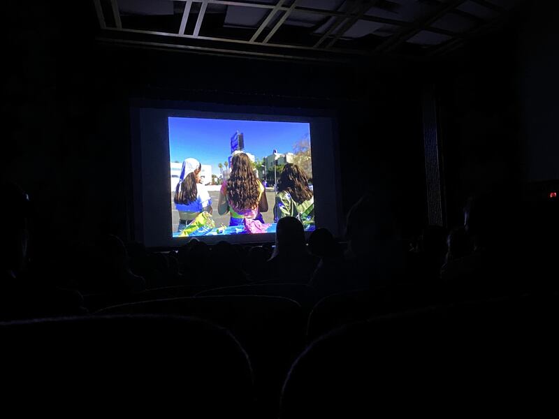 Three girls projected on a screen at a film festival.