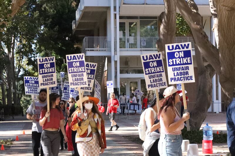 People protest at UCLA, with blue on white signs that say "UAW on strike unfair labor practice"