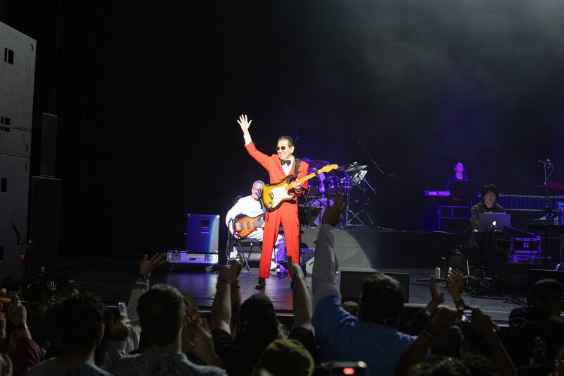 A photo of a man in a red suit with a guitar waving to a crowd